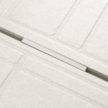 Una cubierta de drenaje lineal se asienta dentro de una rejilla rectangular texturizada de azulejos de colores claros, creando u