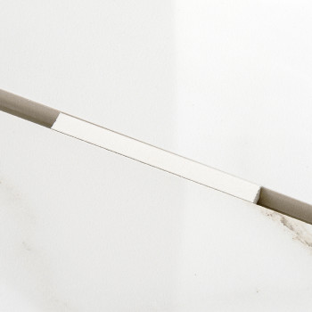 Un carreau rectangulaire blanc repose en diagonale sur une surface beige clair, montrant en dessous des ombres subtiles et des m