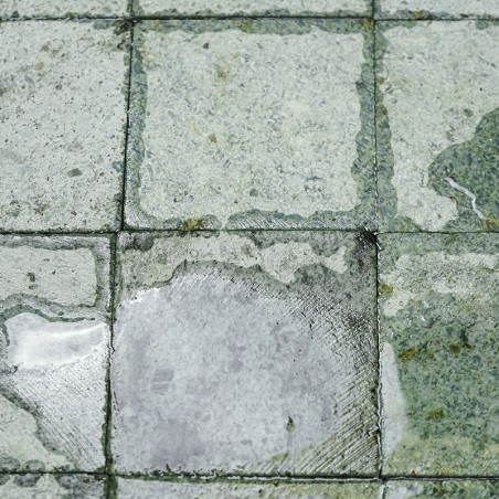 Wet square stone tiles with irregular patterns, reflecting light, arranged in rows creating a textured, outdoor ground surface.
