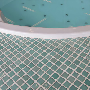 A circular hot tub rests, filled with water, above a patterned floor of square, blue-green glass mosaic tiles.