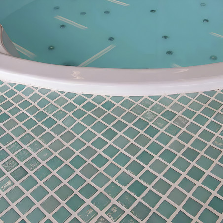 A circular hot tub rests, filled with water, above a patterned floor of square, blue-green glass mosaic tiles.