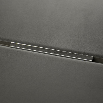 Un carreau gris foncé avec une barre métallique incrustée sur sa surface, réfléchissant la lumière, sur un fond lisse et minimal