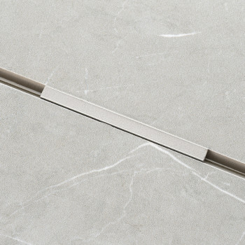 Un carreau rectangulaire gris clair présente un motif de marbre subtil avec de légères veines blanches. Une fine bande métalliqu