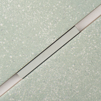 Um ladrilho retangular com um padrão claro salpicado é cruzado diagonalmente por uma faixa fina e elevada, criando um contraste 