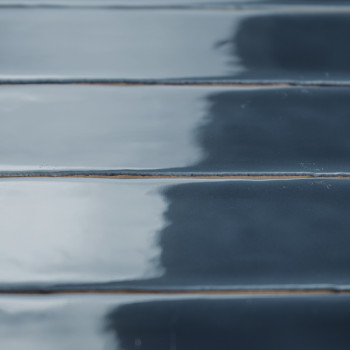Glänzende, rechteckige, dunkelblaue Fliesen liegen in parallelen Reihen und reflektieren das Licht subtil. Sie sorgen für einen 