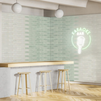 Un bar minimalista cuenta con tres taburetes de madera en un mostrador de concreto. Un letrero de neón dice `KARAOKE BAR` debajo
