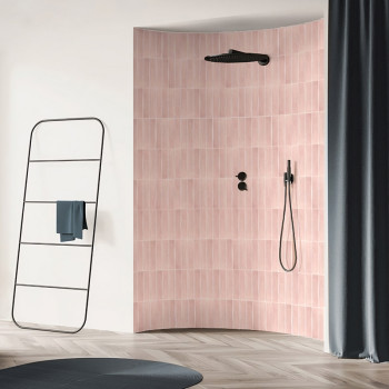 Una pared curva con azulejos rosas sostiene un cabezal de ducha y controles negros, rodeada por un baño moderno con toallero y c