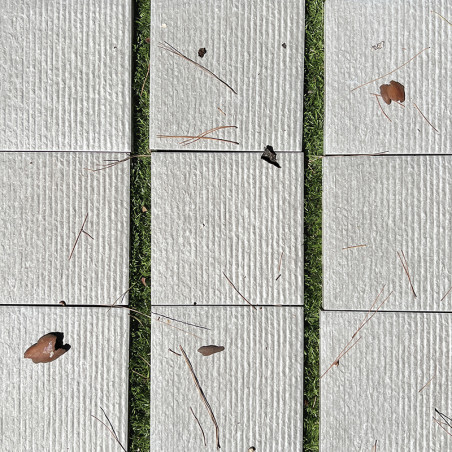 Les carreaux rectangulaires beiges reposent sur de l'herbe, parsemée de feuilles sèches et d'aiguilles de pin, créant un contras