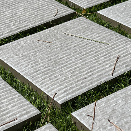 Vierkante stenen tegels liggen gelijkmatig verdeeld op weelderig groen gras, met gestructureerde ruggen met verspreide dunne twi