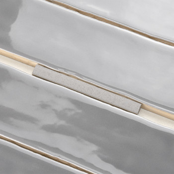 Carreaux gris brillants aux surfaces ondulées et inégales. séparés par de fines lignes de coulis beiges et blanches, créant une 