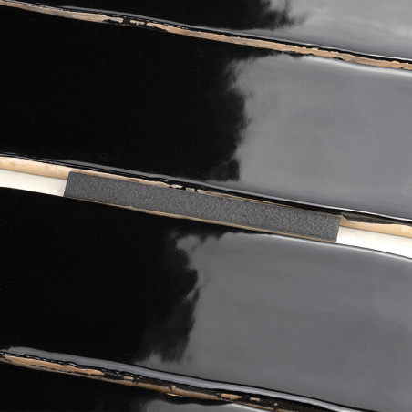Shiny black tiles interlock with uneven edges, reflecting light. A thin, horizontal strip crosses the center, contrasting agains