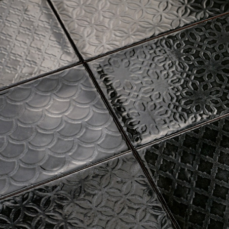 Schwarze, glänzende Fliesen weisen verschiedene Prägemuster auf, darunter Schuppen, Blumenmotive und geometrische Muster, wodurc