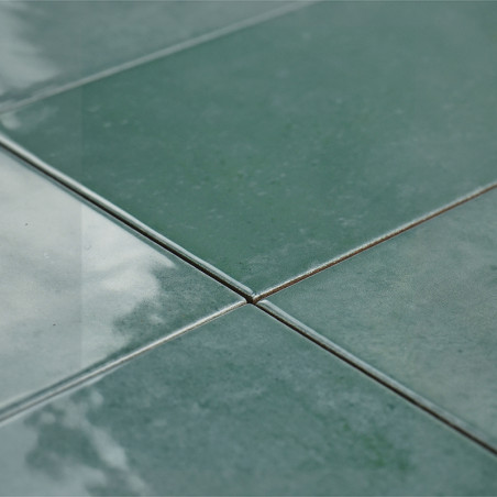 Quatre carreaux verts brillants se rejoignent au centre, réfléchissant la lumière, créant une surface lisse et polie dans un déc