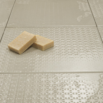 Los azulejos de textura neutra quedan planos y reflejan la luz sutilmente. Dos jabones rectangulares descansan encima, añadiendo