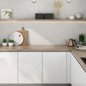 Witte keukenkasten bevinden zich onder een lichthouten aanrechtblad, versierd met potplanten en keukengerei, onder een houten pl