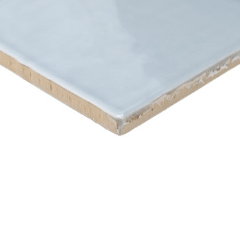 Un azulejo cerámico azul claro brillante con una superficie lisa descansa en ángulo, mostrando su borde beige sin terminar sobre