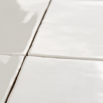 Four glossy, white ceramic tiles form a grid, joined by thin grout lines, reflecting light in a smooth, clean kitchen setting.