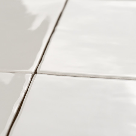 Four glossy, white ceramic tiles form a grid, joined by thin grout lines, reflecting light in a smooth, clean kitchen setting.