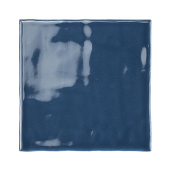 Un azulejo cerámico azul oscuro brillante refleja la luz, mostrando sombras y rayas en su superficie lisa, sobre un fondo liso.