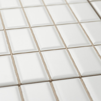 Les carreaux de céramique blanche sont soigneusement disposés selon un motif en grille, légèrement surélevés en leur centre, cré