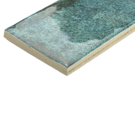 Un azulejo cerámico rectangular presenta una superficie brillante y moteada de color azul verdoso. Se apoya plano, mostrando una