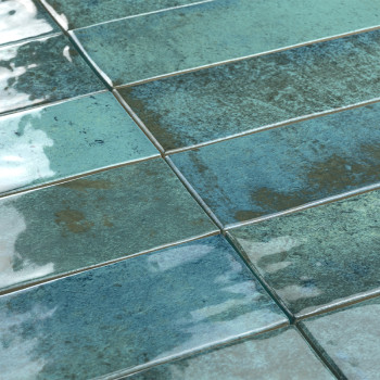 Azulejos rectangulares brillantes en tonos de azul y verde se encuentran uno al lado del otro, reflejando la luz en una superfic