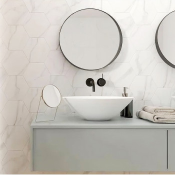 Un miroir rond est accroché au mur d’une salle de bain, au-dessus d’un lavabo blanc moderne. Le cadre comprend une décoration mi