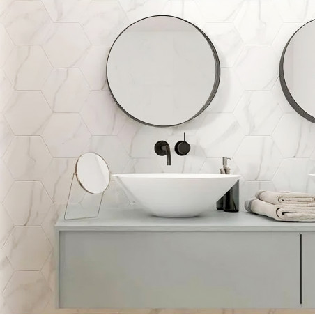 Un miroir rond est accroché au mur d’une salle de bain, au-dessus d’un lavabo blanc moderne. Le cadre comprend une décoration mi