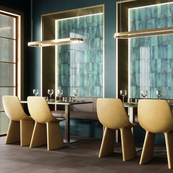 Sillas amarillas rodean una elegante mesa de comedor con cristalería en una habitación moderna con paredes de azulejos verdes e 