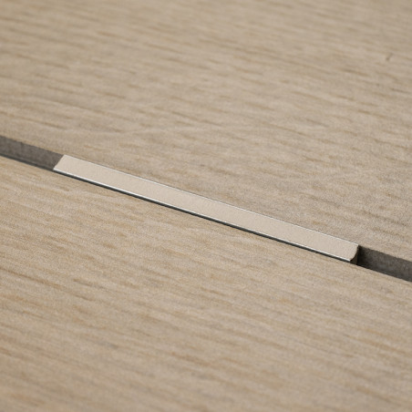 Un carreau beige à texture de bois repose à plat avec une étroite bande métallique encastrée dans une rainure centrale, contre u
