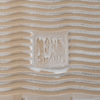 Fliese mit Sandstruktur und der Prägung „MADE IN SPAIN“. Wellenmuster erzeugen einen Welleneffekt und suggerieren eine strandähn