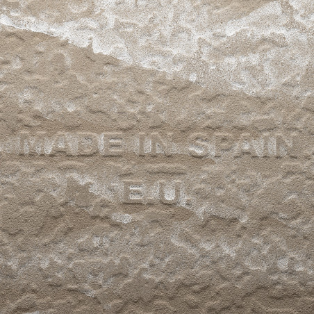 Un azulejo beige texturizado presenta un texto en relieve que dice `MADE IN SPAIN E.U.` en una superficie irregular parecida a u