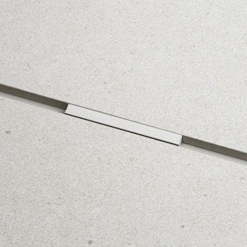 Un azulejo rectangular liso, de color beige claro y con una textura sutil, presenta una delgada tira metálica horizontal en el m