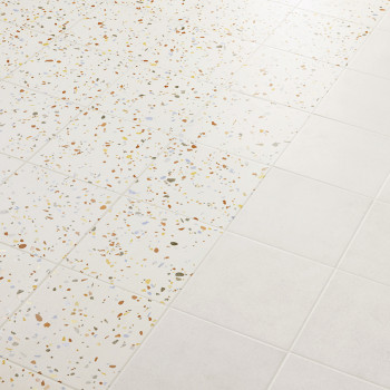 De tegels gaan over van terrazzo, gespikkeld met veelkleurige chips, naar effen wit, waardoor een patroon op het gladde vloeropp
